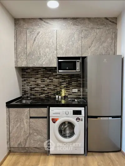 Modern kitchen with sleek cabinetry, washing machine, and stainless steel fridge in compact layout.