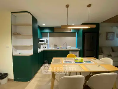 Modern kitchen with green cabinets and dining area, featuring a sleek design and contemporary lighting.