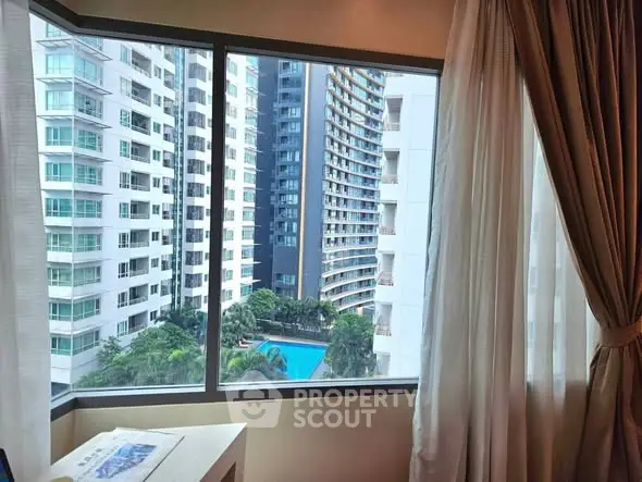 Stunning urban view from high-rise apartment window with pool and modern buildings.
