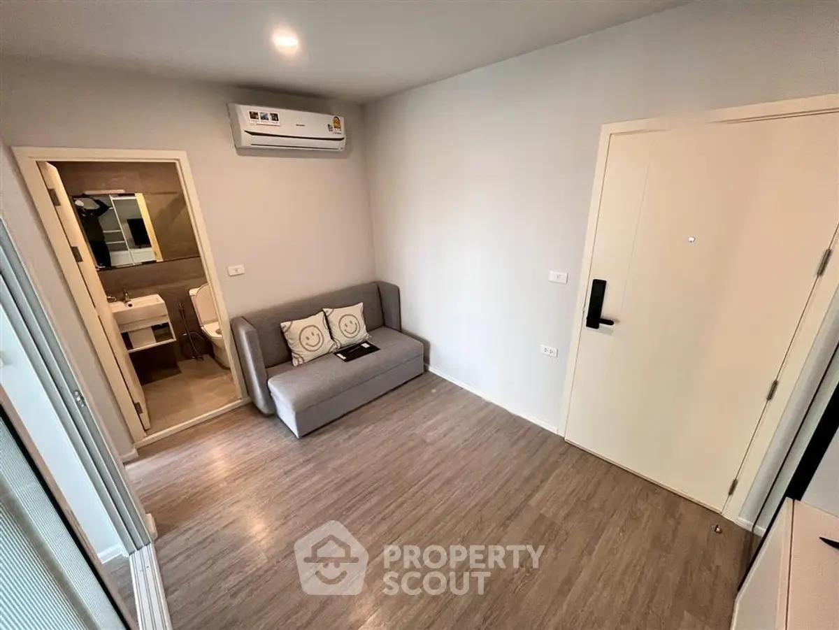 Modern apartment interior with compact living room and view into bathroom, featuring sleek design and wooden flooring.