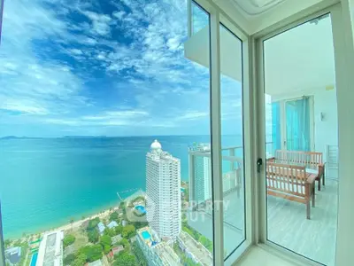 Stunning ocean view from high-rise balcony with modern glass doors and seating area.