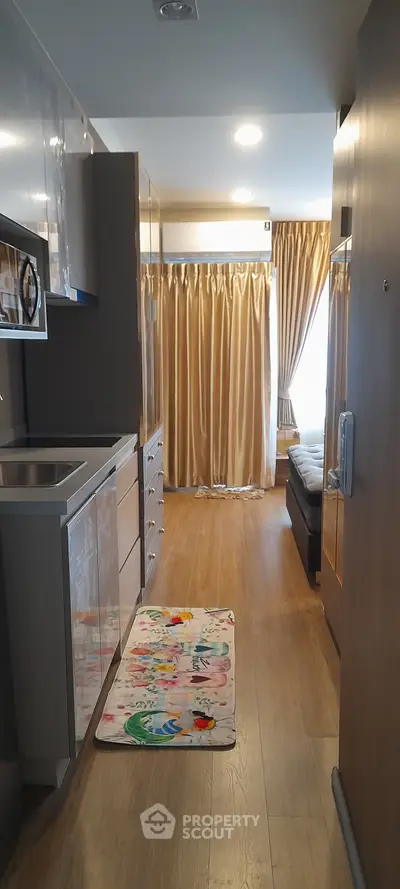 Modern apartment interior with open kitchen and cozy living area, featuring elegant curtains and wooden flooring.