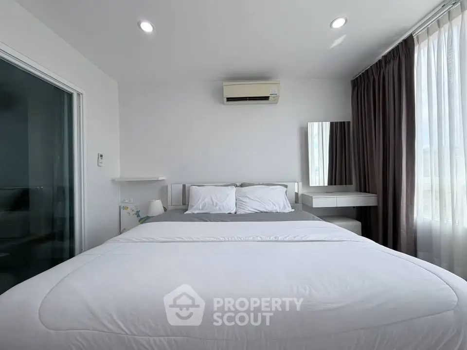 Modern bedroom with white bedding, air conditioning, and natural light from large windows.