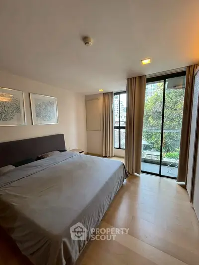 Spacious bedroom with large windows and balcony view in modern apartment.