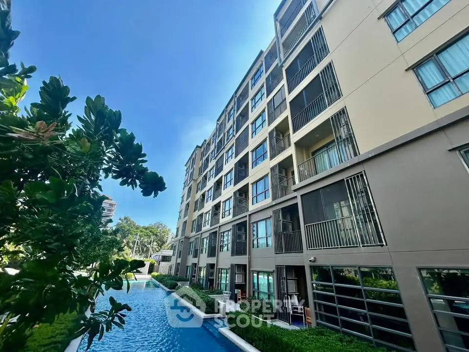 Modern apartment building with pool and lush greenery under clear blue sky.