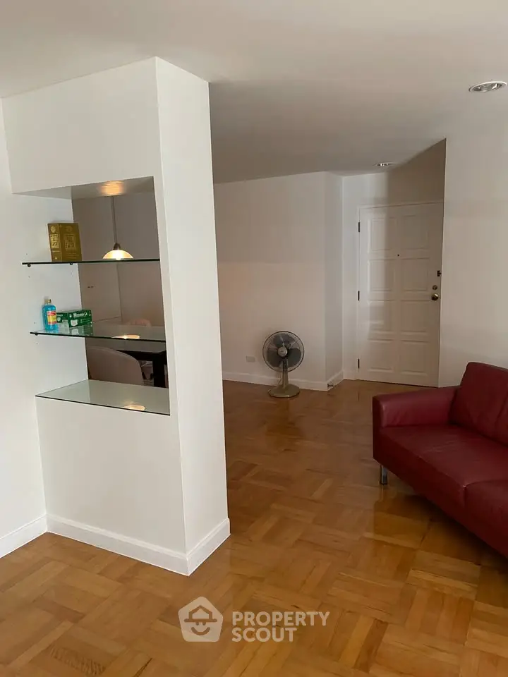 Spacious living room with parquet flooring and modern red sofa, ideal for stylish urban living.