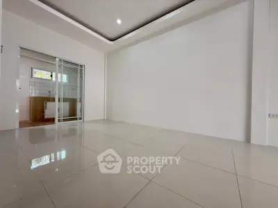 Spacious modern living room with sleek tile flooring and sliding glass doors leading to a bright kitchen.