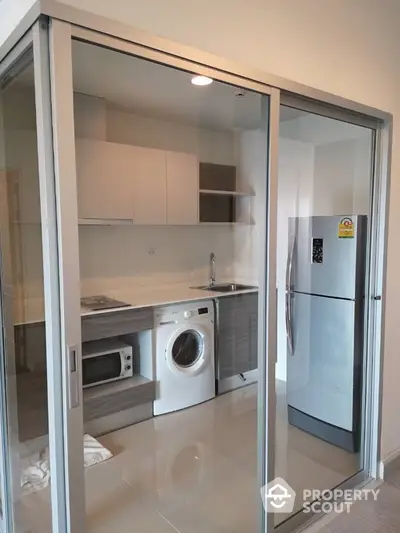 Modern kitchen with glass sliding doors, featuring washing machine and stainless steel fridge.