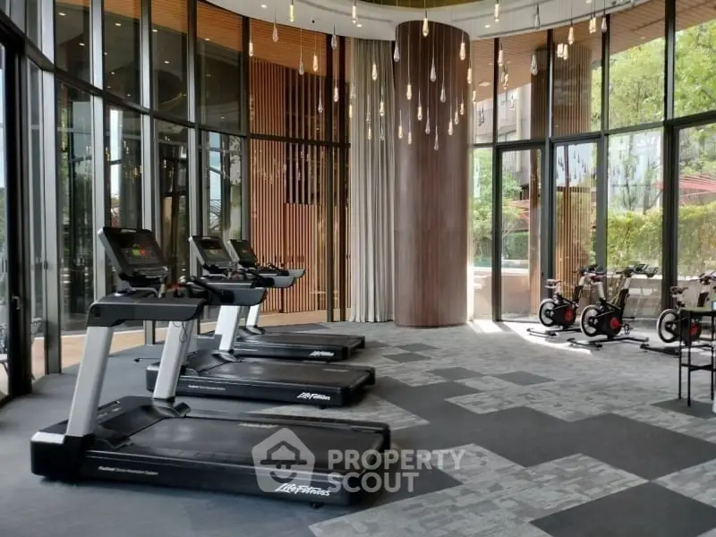 Luxurious gym with modern equipment and floor-to-ceiling windows offering garden views.