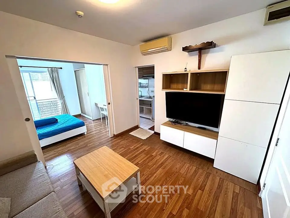 Modern living room with wooden flooring, open layout, and view into bedroom