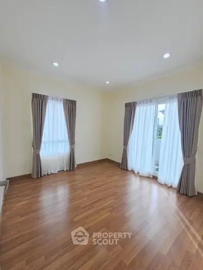 Spacious empty room with wooden flooring and large windows, perfect for customization.