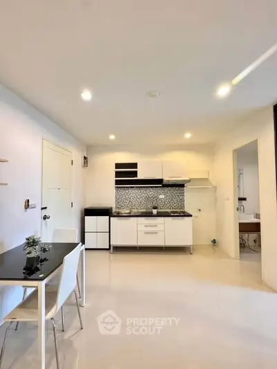Modern kitchen with sleek white cabinets and dining area in open layout apartment.