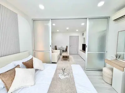 Modern bedroom with sliding doors leading to a stylish living area, featuring neutral tones and elegant decor.