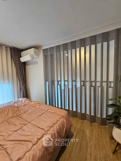 Cozy bedroom with modern decor and large window, featuring elegant curtains and a stylish air conditioning unit.