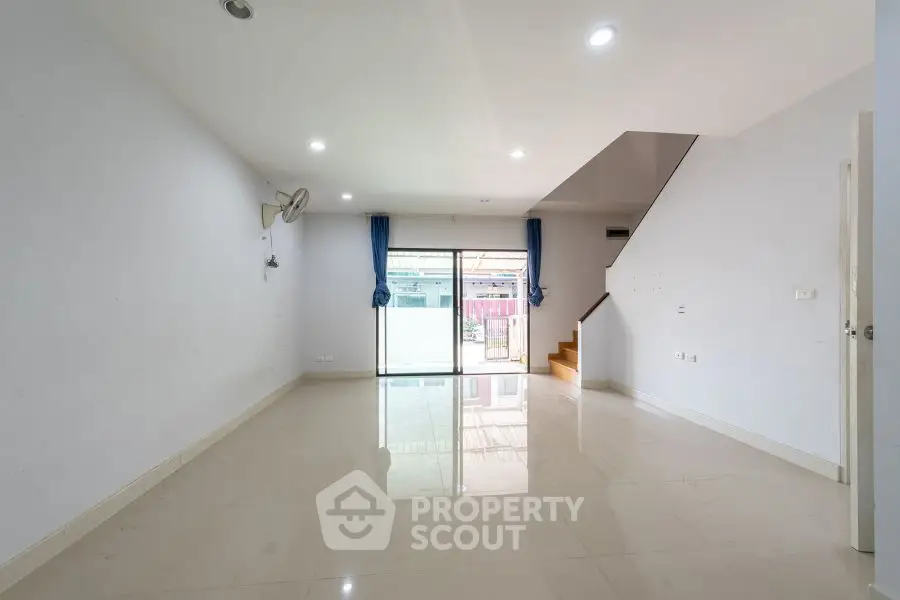 Spacious empty living room with large windows and staircase, ideal for customization.