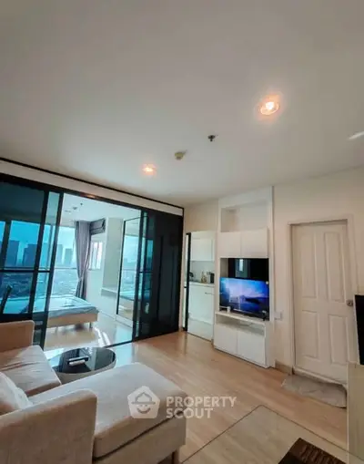 Modern living room with glass doors leading to a bedroom, featuring cozy seating and a sleek TV setup.