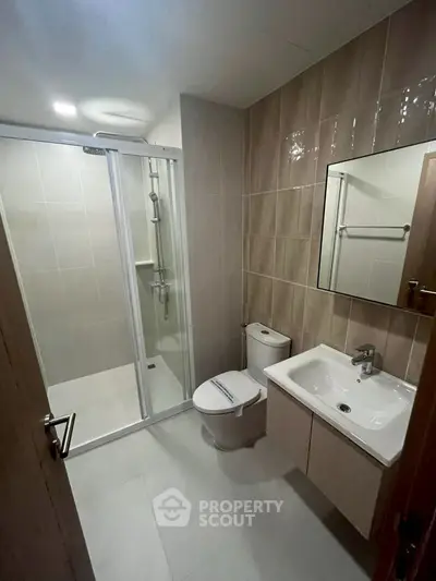 Modern bathroom with glass shower, sleek sink, and neutral tiles.