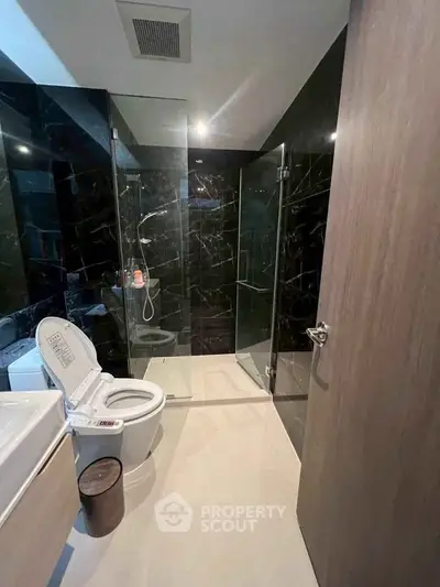 Luxurious modern bathroom with sleek black tiles and glass shower enclosure.