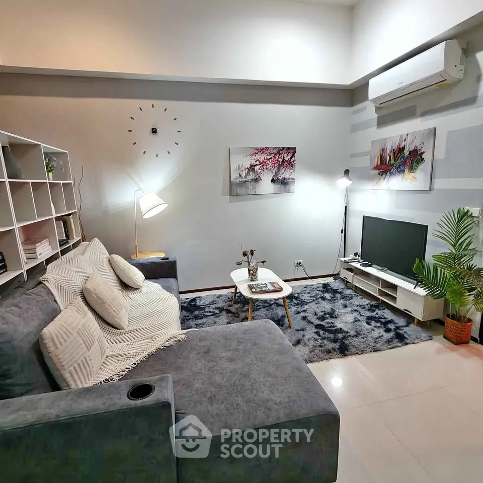 Stylish modern living room with cozy gray sofa, chic decor, and wall-mounted air conditioning.