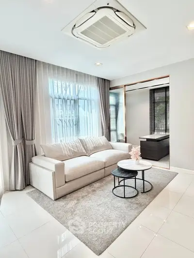 Modern living room with elegant sofa and stylish decor, featuring large windows and soft lighting.