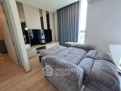 Modern living room with stylish gray sofa and large TV, featuring elegant decor and natural light.