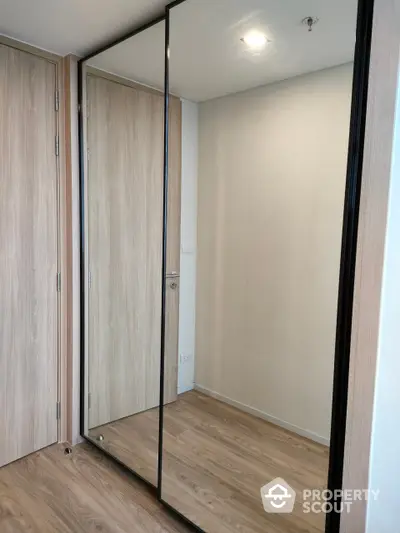 Modern minimalist bedroom with large mirrored wardrobe doors reflecting a spacious feel, complemented by sleek wooden flooring.