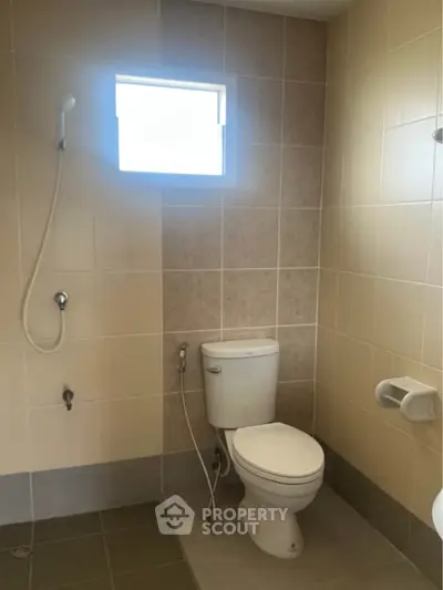 Modern bathroom with tiled walls and a window, featuring a toilet and shower area.