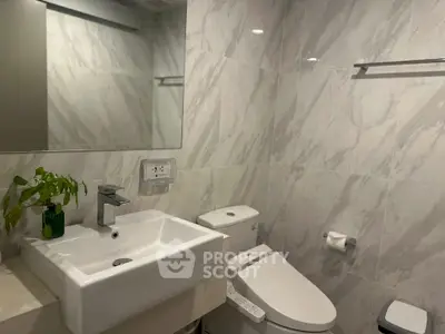 Modern bathroom with sleek fixtures and marble walls, featuring a stylish sink and toilet.