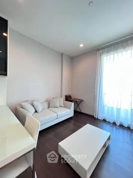 Modern living room with white sofa, sleek coffee table, and large window with sheer curtains.
