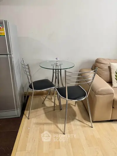 Cozy living area with modern glass table, chairs, and fridge, perfect for compact urban living.