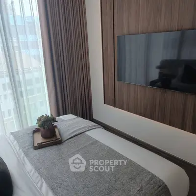 Modern bedroom with stylish decor and wall-mounted TV, featuring large window with city view.