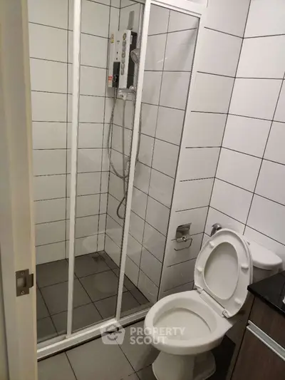 Modern bathroom with shower and toilet in sleek white tile design.
