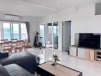 Spacious modern living room with dining area and exercise bike, perfect for family gatherings.