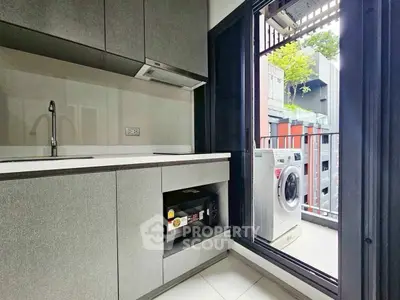Modern kitchen with balcony and washing machine, sleek cabinetry and open layout.
