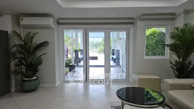 Spacious living room with large glass doors opening to a lush garden view, featuring modern decor and natural light.