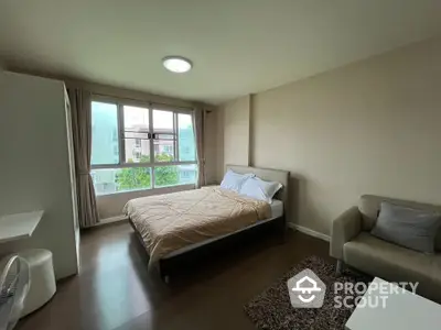 Spacious bedroom with large window and modern furnishings in a cozy apartment.