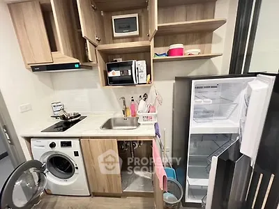 Compact kitchen with modern appliances including washing machine and open fridge.