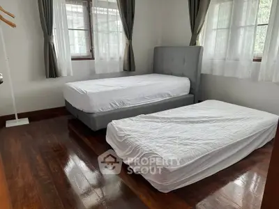 Spacious bedroom with two beds and polished wooden floors, ample natural light from large windows.