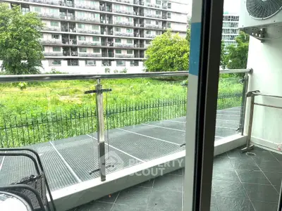 Spacious balcony with modern railing overlooking lush greenery and urban buildings.