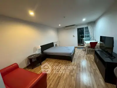 Spacious studio apartment with modern furnishings and wooden flooring, featuring a cozy living area and large window.