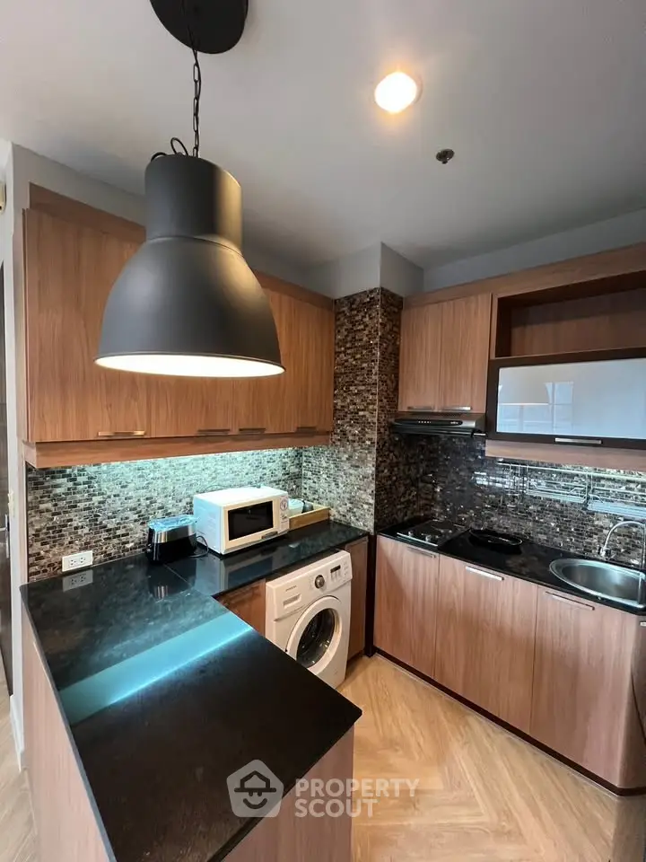 Modern kitchen with wood cabinets, washing machine, and sleek black countertops.