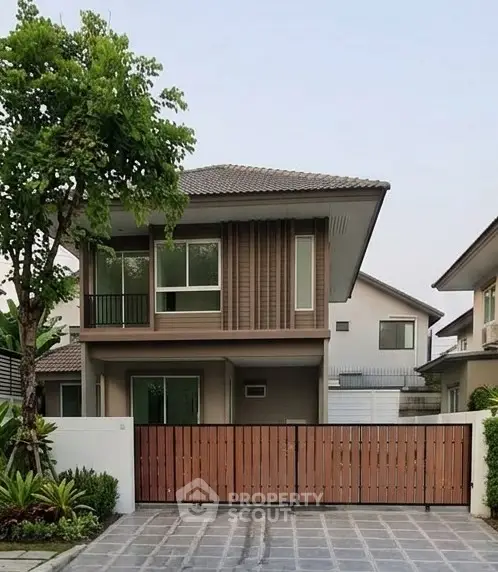 Modern two-story house with gated entrance and lush greenery