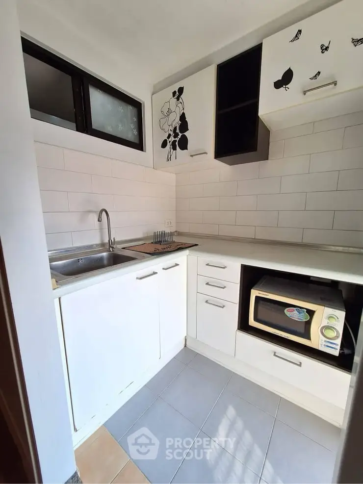 Compact kitchen with modern white cabinets and microwave, ideal for efficient cooking.