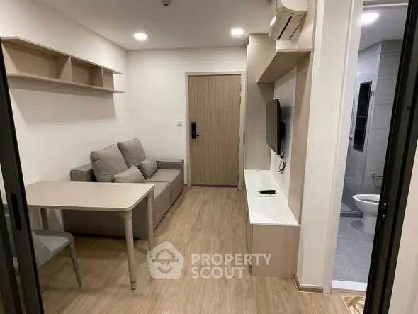Modern compact living room with cozy sofa, wall-mounted TV, and adjacent bathroom in stylish apartment.