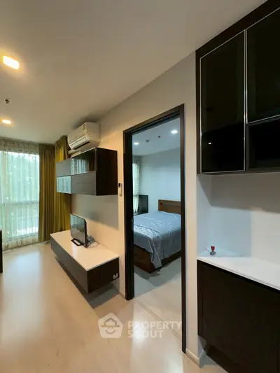 Modern apartment interior with living room and bedroom view, featuring sleek furniture and natural lighting.