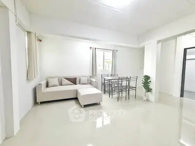 Spacious living room with modern furniture and dining area in bright, minimalist apartment.