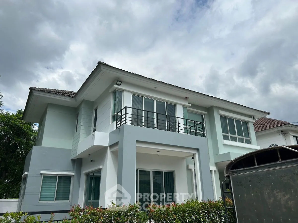 Modern two-story house with large windows and balcony under cloudy sky.