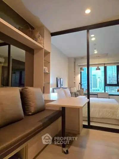 Modern studio apartment with city view, featuring a cozy seating area and sliding glass doors.