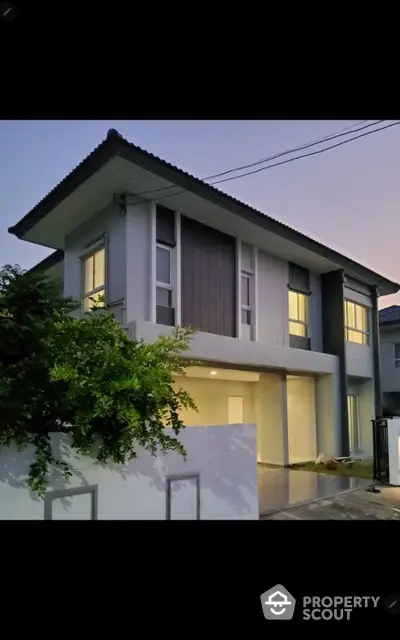 Modern two-story house with sleek design and lush greenery at dusk