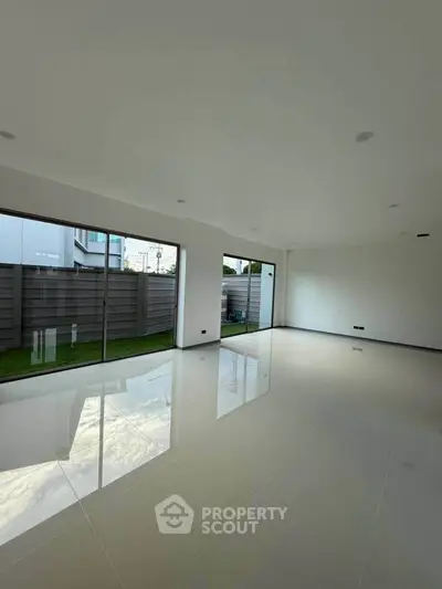 Spacious modern living room with large windows and glossy tiled floors, offering a bright and airy ambiance.